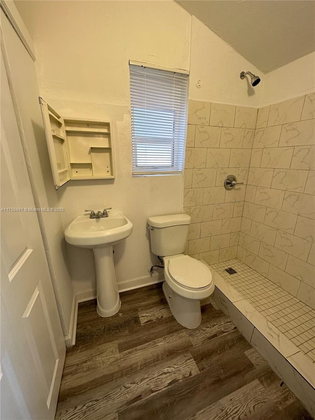 bathroom with lofted ceiling, a tile shower, toilet, and wood finished floors