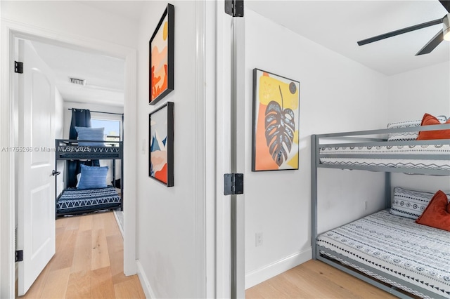 bedroom featuring light wood-style flooring, a ceiling fan, visible vents, and baseboards