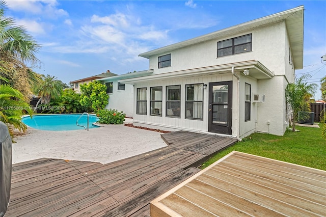 rear view of property featuring a wooden deck, central AC unit, a fenced in pool, a yard, and stucco siding