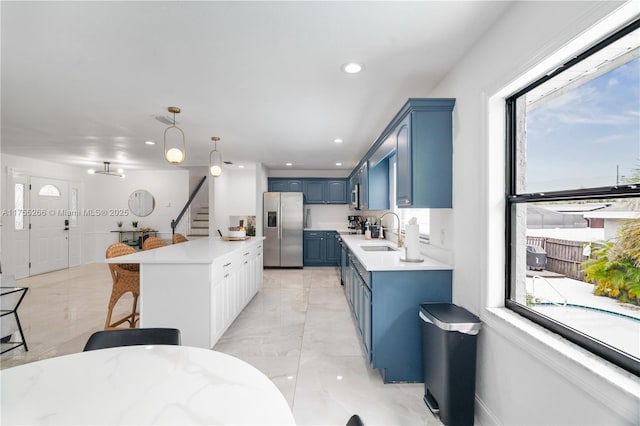 kitchen with stainless steel fridge, blue cabinets, light countertops, a sink, and recessed lighting