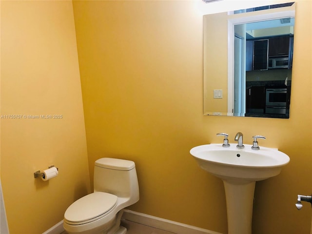 bathroom with toilet, visible vents, baseboards, and a sink