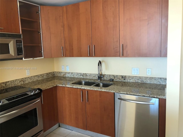 kitchen featuring brown cabinetry, appliances with stainless steel finishes, light stone counters, a sink, and light tile patterned flooring