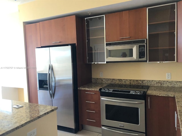 kitchen featuring brown cabinets, light stone countertops, glass insert cabinets, and stainless steel appliances