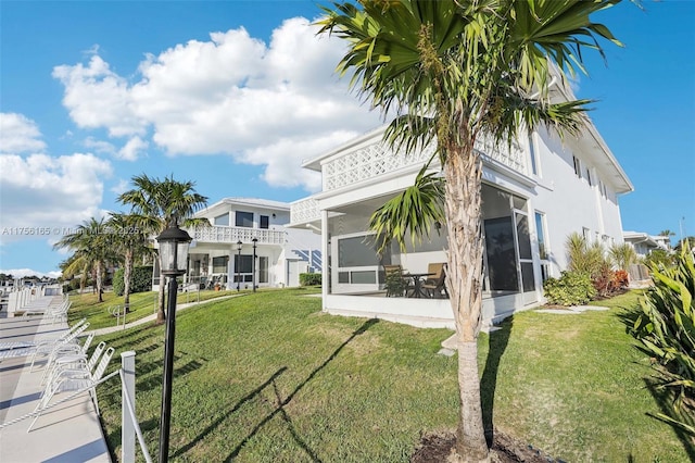 back of property featuring a sunroom, a yard, and stucco siding