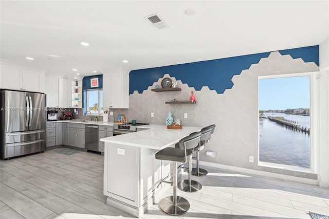 kitchen featuring open shelves, light countertops, visible vents, appliances with stainless steel finishes, and a peninsula