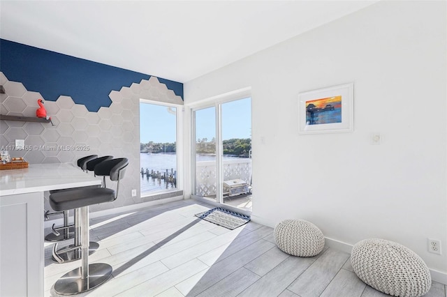 interior space with light wood-type flooring, a water view, and baseboards