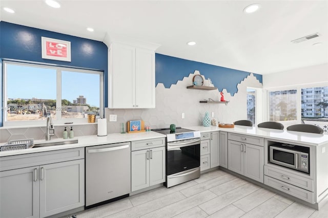 kitchen featuring gray cabinets, visible vents, appliances with stainless steel finishes, a sink, and a peninsula