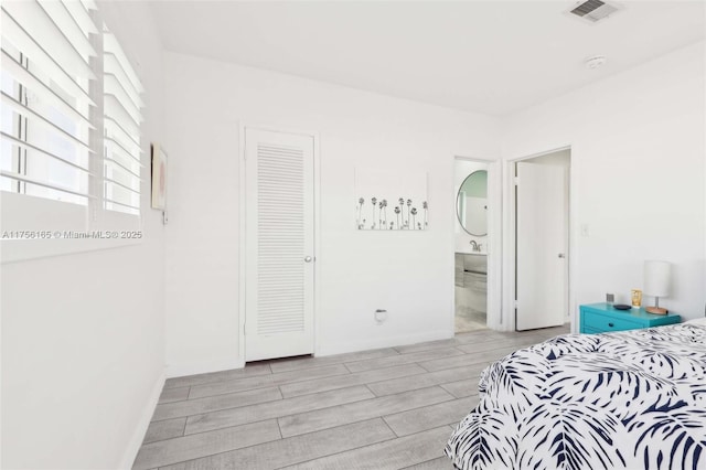 bedroom with wood tiled floor, visible vents, ensuite bath, and baseboards