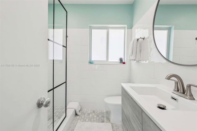 full bath featuring a tile shower, tile walls, toilet, and vanity