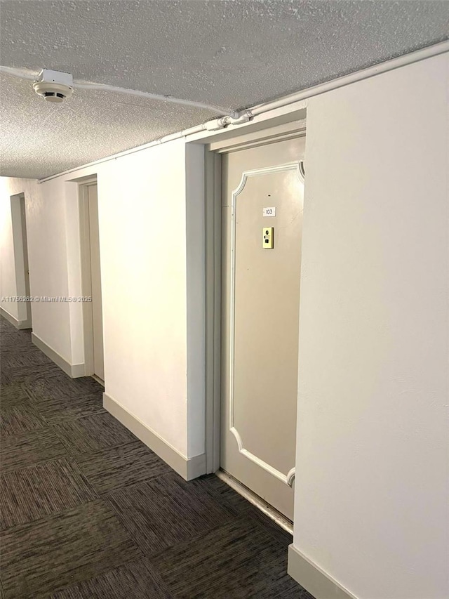 hallway with a textured ceiling, carpet floors, and baseboards