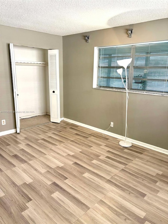 unfurnished bedroom with light wood-type flooring, a closet, a textured ceiling, and baseboards