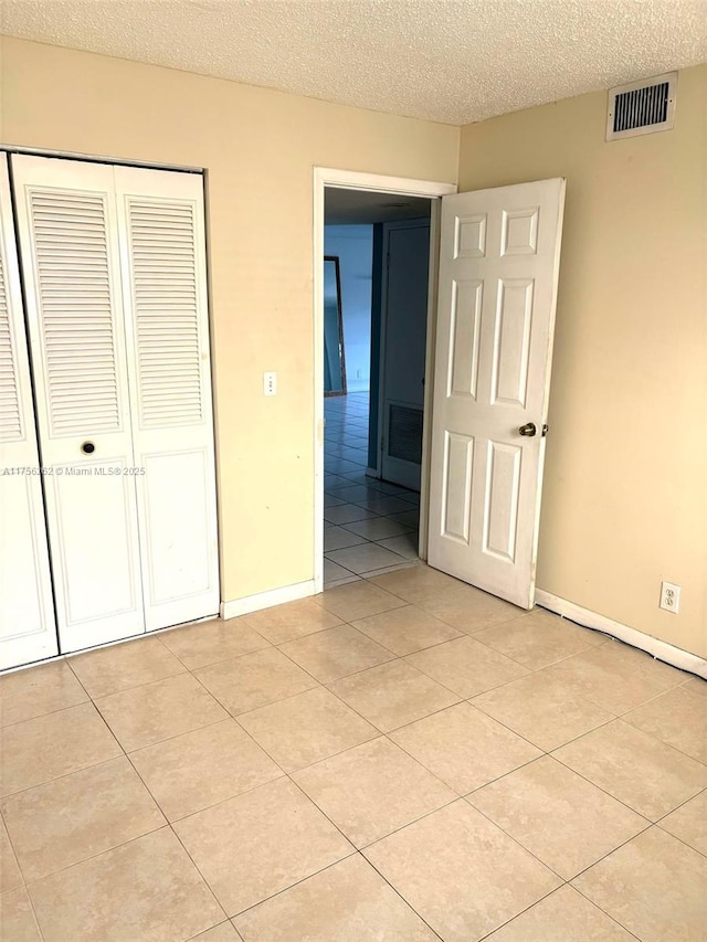 unfurnished bedroom featuring a closet, visible vents, light tile patterned flooring, a textured ceiling, and baseboards