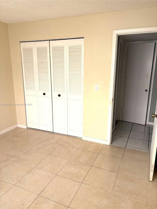 unfurnished bedroom featuring a closet, a textured ceiling, baseboards, and light tile patterned floors