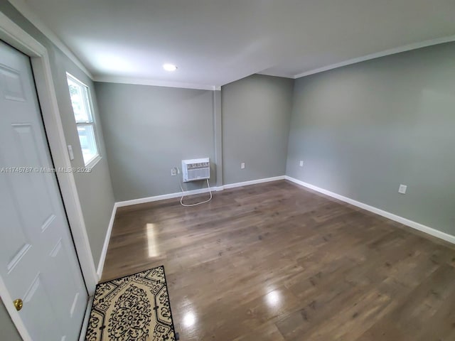 empty room featuring an AC wall unit, crown molding, baseboards, and wood finished floors