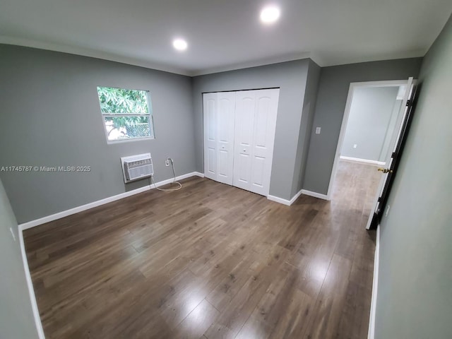 unfurnished bedroom featuring dark wood finished floors, recessed lighting, a closet, an AC wall unit, and baseboards