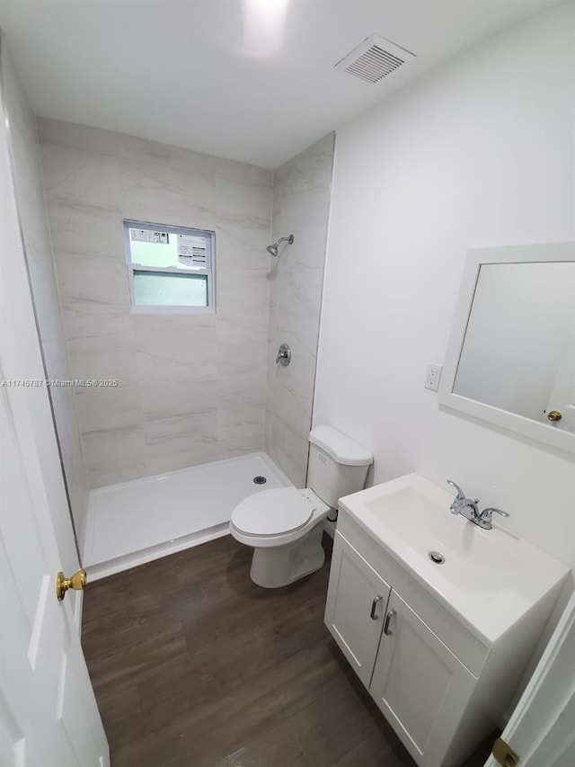 bathroom with visible vents, toilet, a tile shower, vanity, and wood finished floors