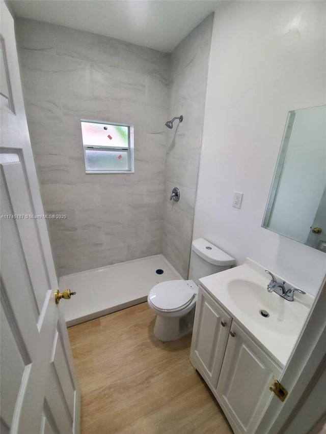 full bath featuring a tile shower, vanity, wood finished floors, and toilet