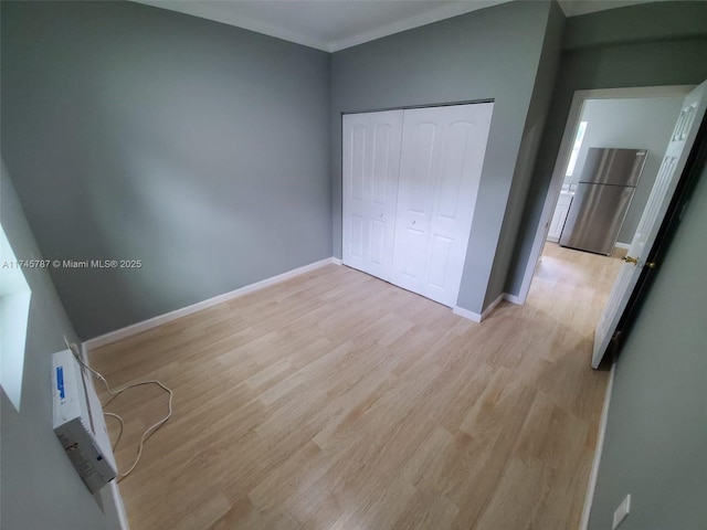 unfurnished bedroom with light wood-style floors, baseboards, a closet, and freestanding refrigerator