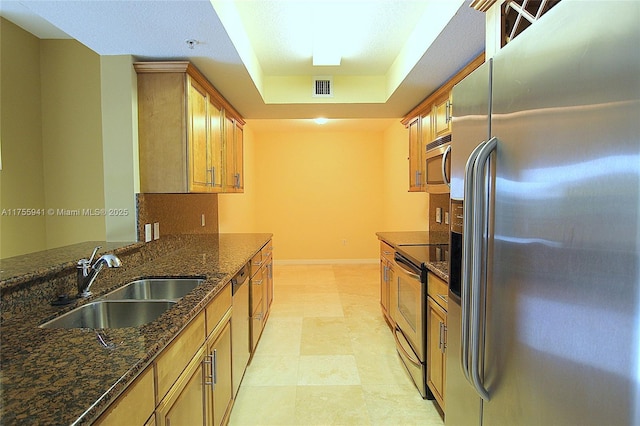 kitchen featuring a tray ceiling, visible vents, appliances with stainless steel finishes, a sink, and dark stone countertops