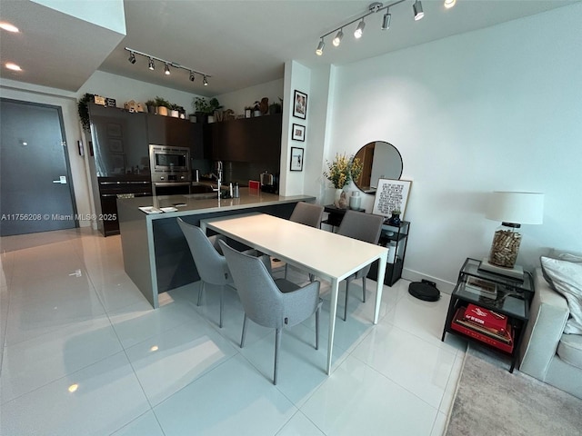 kitchen featuring light tile patterned floors, a peninsula, a sink, appliances with stainless steel finishes, and rail lighting