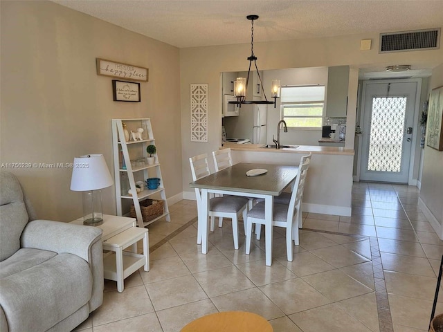 dining space with light tile patterned floors, a textured ceiling, a notable chandelier, visible vents, and baseboards