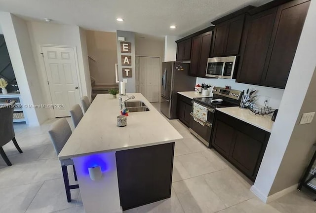 kitchen with a center island with sink, a breakfast bar, stainless steel appliances, light countertops, and a sink