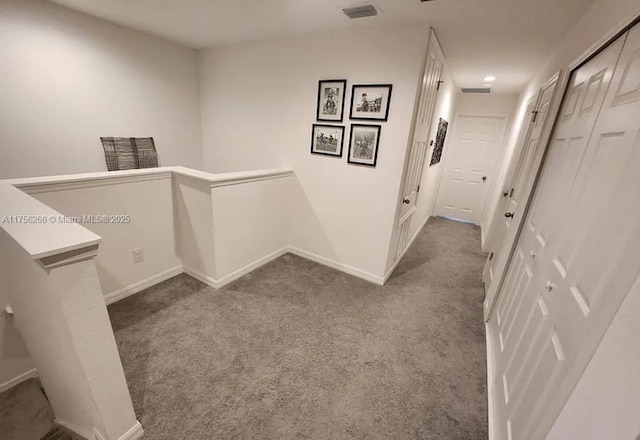 hallway with carpet floors, baseboards, visible vents, and an upstairs landing