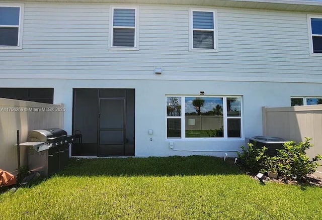 back of property with central air condition unit, fence, a lawn, and stucco siding