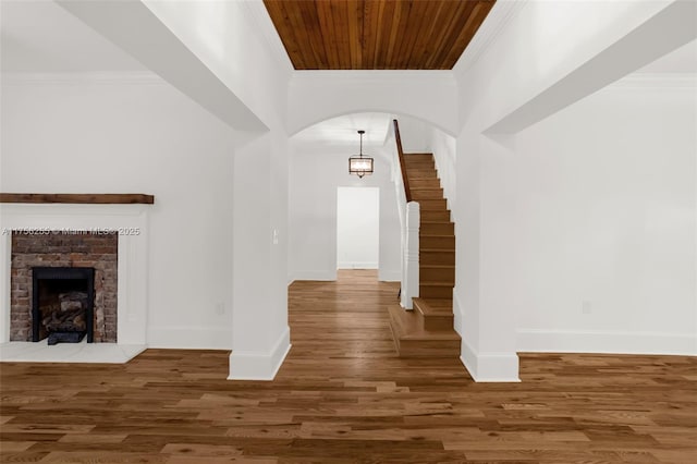 foyer entrance featuring arched walkways, wood finished floors, stairs, ornamental molding, and a brick fireplace