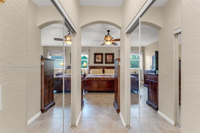 corridor featuring light tile patterned floors, a textured wall, and arched walkways