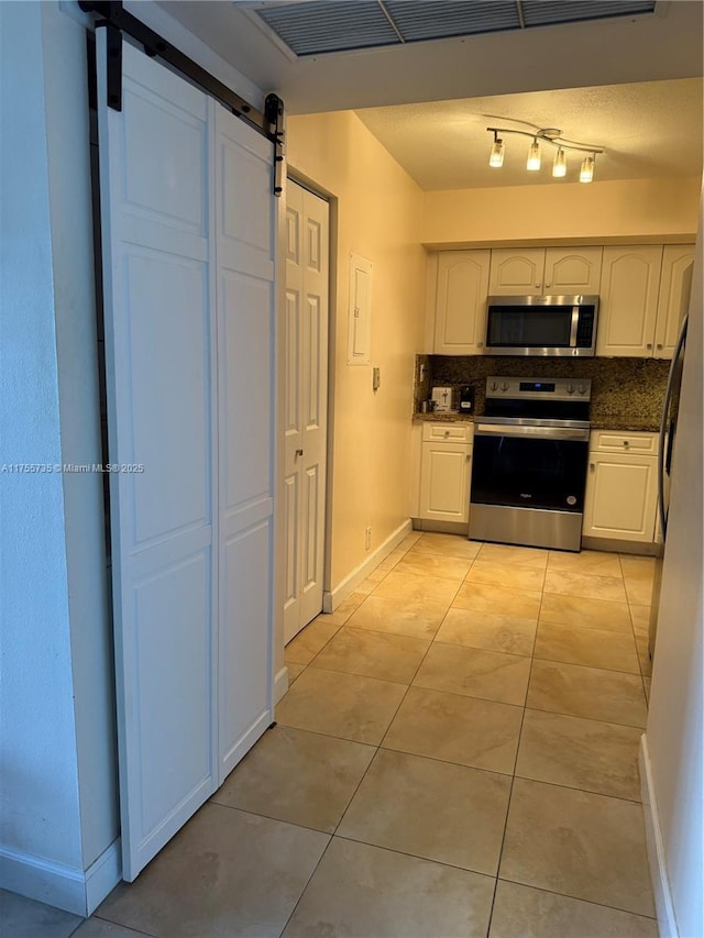 kitchen with light tile patterned floors, a barn door, stainless steel appliances, white cabinets, and tasteful backsplash