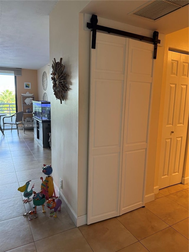 interior space featuring light tile patterned floors, visible vents, baseboards, and a barn door