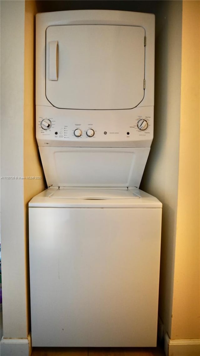 washroom with stacked washer / drying machine, laundry area, and baseboards