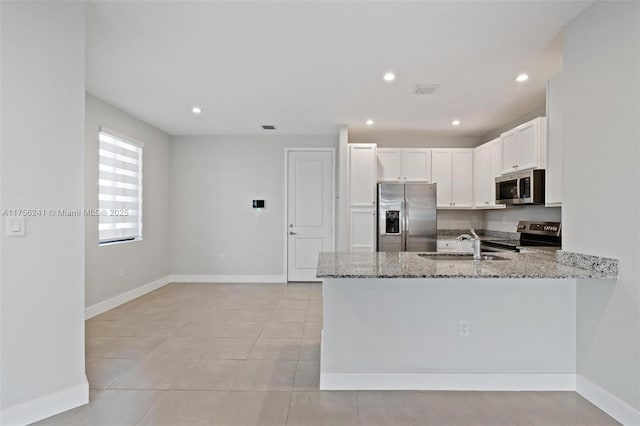 kitchen with light stone counters, a peninsula, white cabinets, stainless steel appliances, and a sink