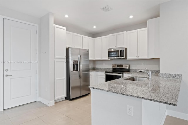 kitchen featuring light stone countertops, visible vents, a peninsula, a sink, and appliances with stainless steel finishes