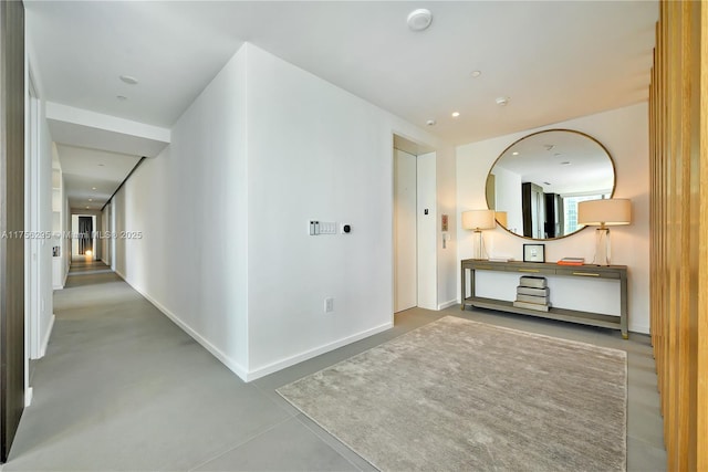 corridor with recessed lighting, finished concrete flooring, and baseboards