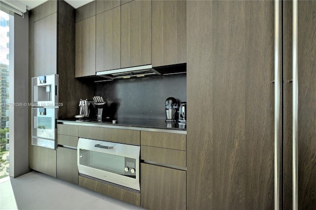 kitchen featuring modern cabinets, oven, black electric stovetop, under cabinet range hood, and backsplash