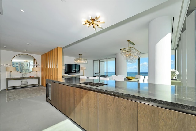 kitchen with a notable chandelier, a sink, brown cabinets, dark stone counters, and decorative light fixtures