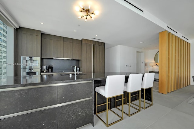 kitchen with a breakfast bar, double oven, a sink, dark stone countertops, and modern cabinets