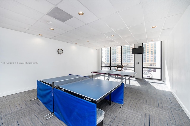 recreation room with a paneled ceiling, expansive windows, baseboards, and carpet floors