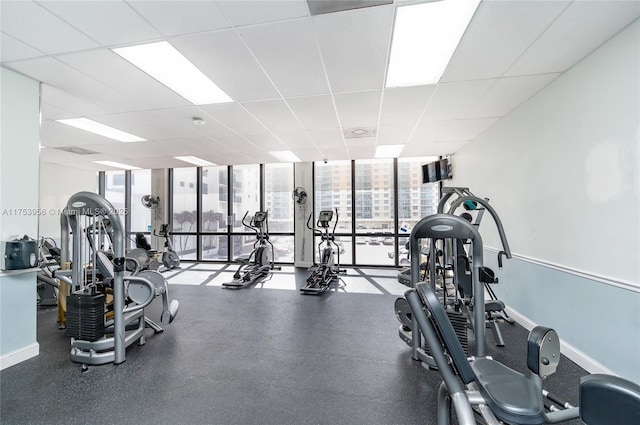 gym featuring a wall of windows, a drop ceiling, and baseboards