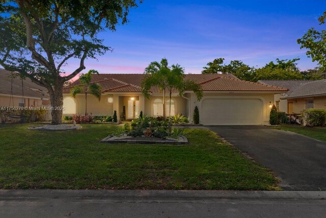 mediterranean / spanish home featuring a garage, driveway, a front lawn, and stucco siding