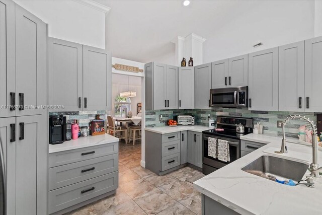 kitchen featuring lofted ceiling, gray cabinetry, a sink, appliances with stainless steel finishes, and tasteful backsplash