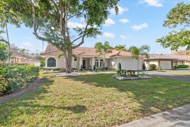 mediterranean / spanish house featuring an attached garage, a tiled roof, driveway, stucco siding, and a front yard