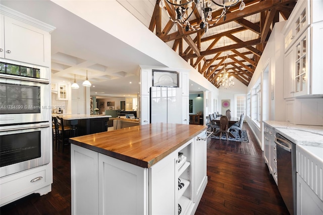 kitchen with a notable chandelier, butcher block countertops, a kitchen island, appliances with stainless steel finishes, and beamed ceiling