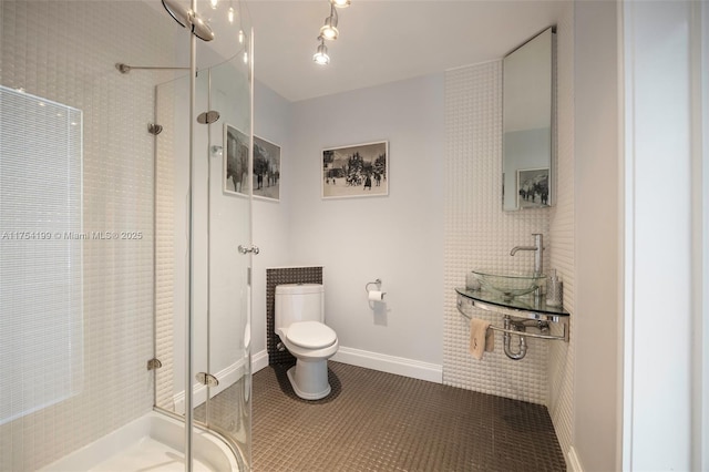 bathroom featuring toilet, a stall shower, a sink, baseboards, and tile patterned floors