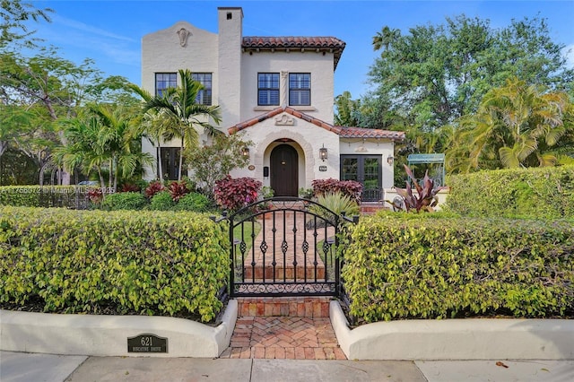 mediterranean / spanish home featuring a tile roof, a gate, a chimney, and stucco siding