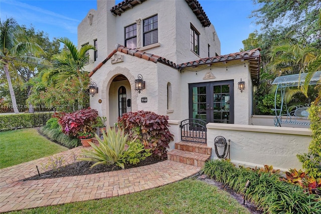 mediterranean / spanish-style house featuring stucco siding, a tiled roof, and french doors