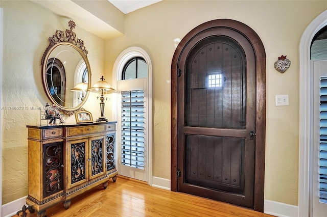 foyer entrance with baseboards, arched walkways, and wood finished floors