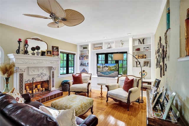 living room with wood finished floors, a ceiling fan, built in features, ornamental molding, and a tiled fireplace